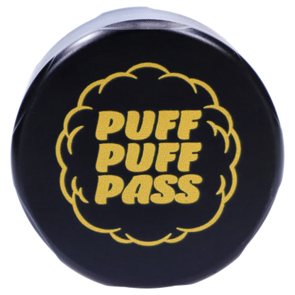 Top-down view of the black Puff Puff Pass Strains OG Kush Grinder-Black showing a gold "PUFF PUFF PASS" puff-shaped logo centered on the lid.