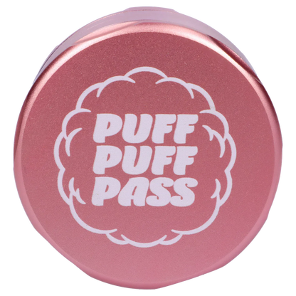 Top-down close-up of the light pink Puff Puff Pass Strains Pink Kush Grinder-Light Pink lid showing bold white "PUFF PUFF PASS" text inside a cloud motif.