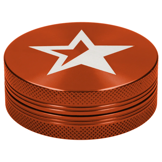 Close-up, angled top view of the orange Famous X Lava 2 pc Grinder - Orange-55mm showing a white star motif on the textured metal lid and knurled sides.