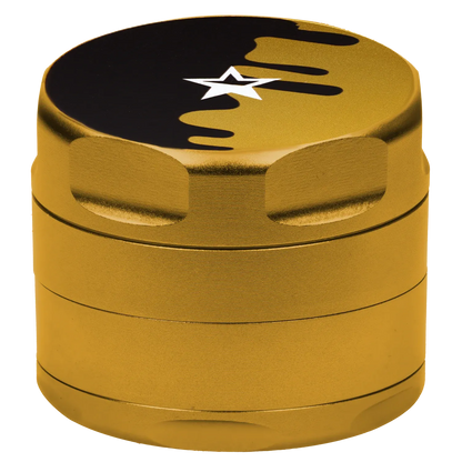 Close-up, slightly elevated view of the gold Famous Design Surrender Aluminum 4 pc Grinder showing its textured sides and star-topped lid with a black drip design.