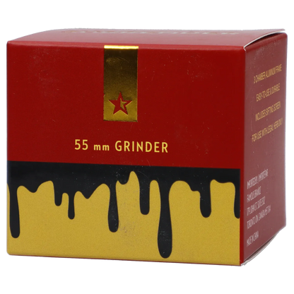 Angled close-up of the red and gold box reading "Famous Design Surrender Aluminum 4 pc Grinder - Gold" with a gold star strip and black drips over yellow.
