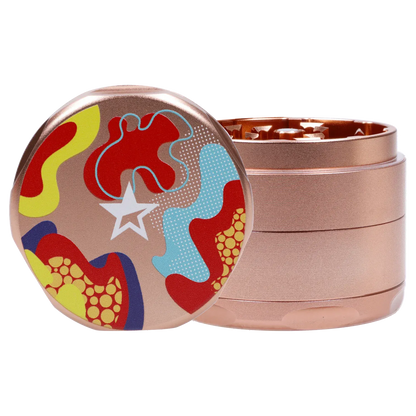 Close-up three-quarter view of the Famous Design Papaya Aluminum 4pc Grinder - Rose Gold showing its colorful abstract top art and stacked metallic rose-gold chambers.