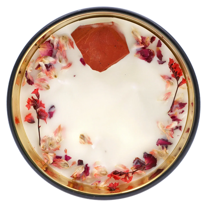 Top-down view of the Queen of Bud: Passion Ritual Box – Candle, Zippo, and Crystal showing a white wax candle rimmed with dried pink and red flower petals and a single red crystal fragment.