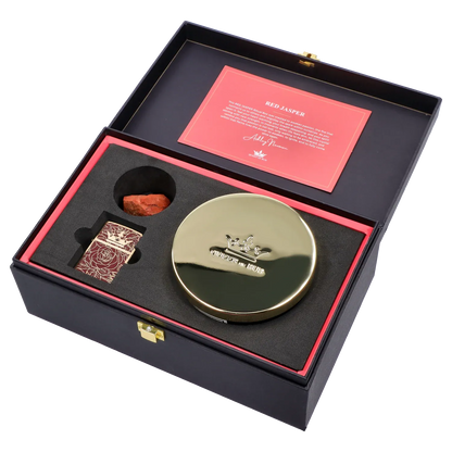 Angled top-down view of the Queen of Bud: Passion Ritual Box – Candle, Zippo, and Crystal inside a black box with red card, gold round candle tin, patterned Zippo, and red jasper stone