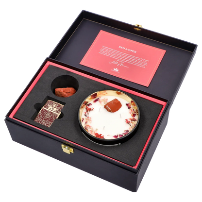 Angled top-down view of the Queen of Bud: Passion Ritual Box – Candle, Zippo, and Crystal open in a black box showing a white floral-trimmed candle with a red jasper stone, a matching red card, and a patterned Zippo insert.