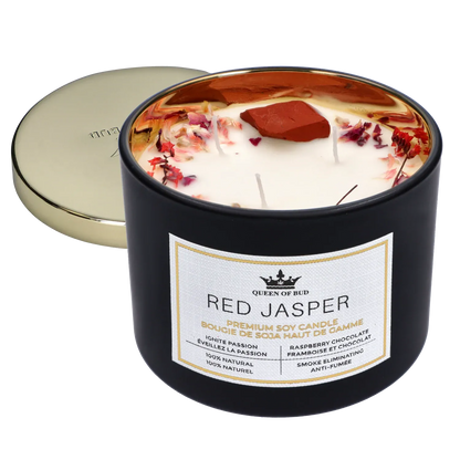 Angled close-up of the Queen of Bud: Passion Ritual Box – Candle, Zippo, and Crystal showing a black tin candle with white wax, dried rose petals and a red jasper stone inside, and a gold lid set behind.