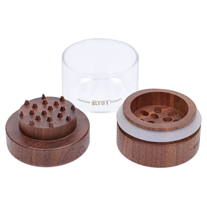 Close-up, top-down view of the disassembled RYOT - GR8TR Walnut Wood Top Grinder w/ Clear Glass Jar Body - 3 inch showing two walnut wooden halves with teeth and a clear glass jar labeled RYOT behind them.