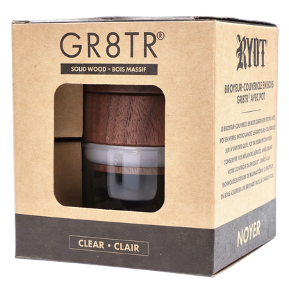Angled close-up of the RYOT - GR8TR Walnut Wood Top Grinder w/ Clear Glass Jar Body - 3 inch visible through its cardboard window.
