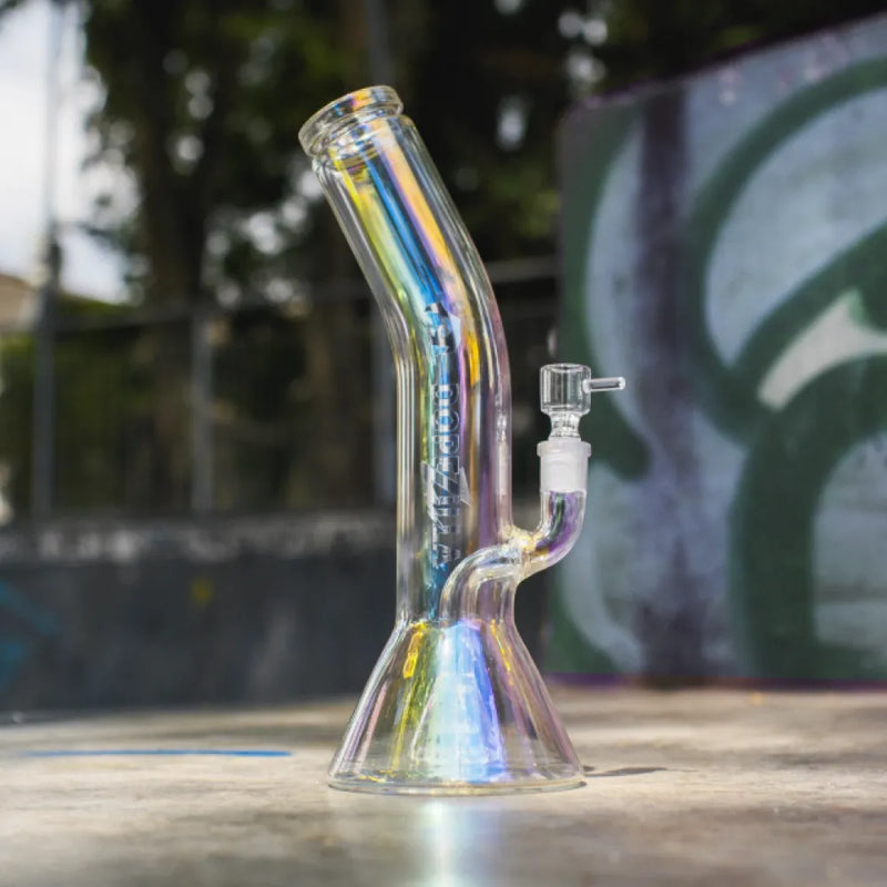 Dopezilla Elemental iridescent glass beaker bong with angled neck and removable bowl sitting on a concrete surface