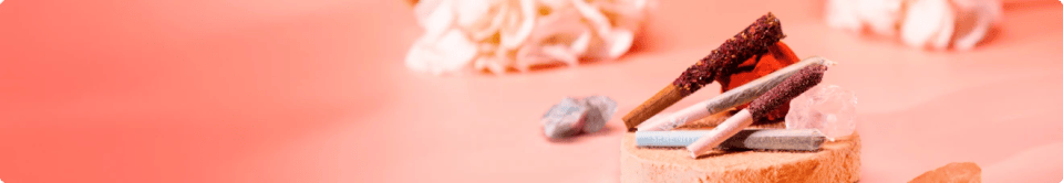 QOB pre-rolls displayed on a small wooden stand with crystals and floral accents against a pink background