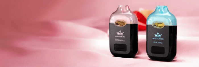 Two compact QOB vapes labeled "Queen of Bud Rose Quartz" and "Queen of Bud Blue Topaz" standing on a soft pink surface