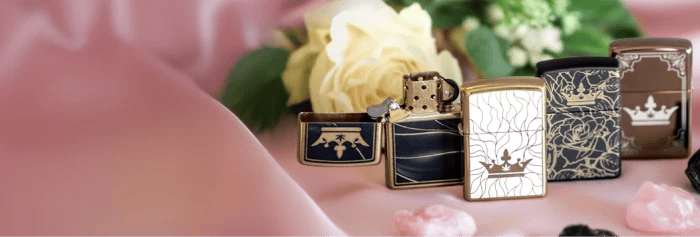 Row of QOB Zippo-style lighters with floral and crown designs displayed on pink satin with a blurred white rose background